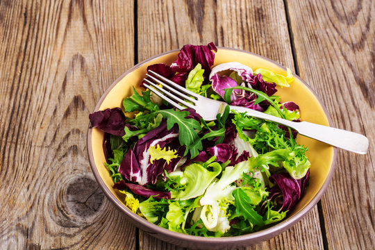 Frise, batavian, radichchio, arugula in a ceramic bowl on a wood