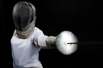 Portrait of fencer woman wearing white fencing costume practicing with the sword. Isolated on black...