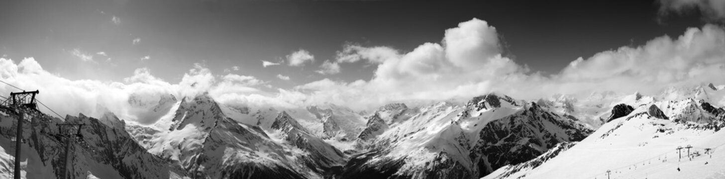Fototapeta Black and white panoramic view on ski slope and cloudy mountains at sun day