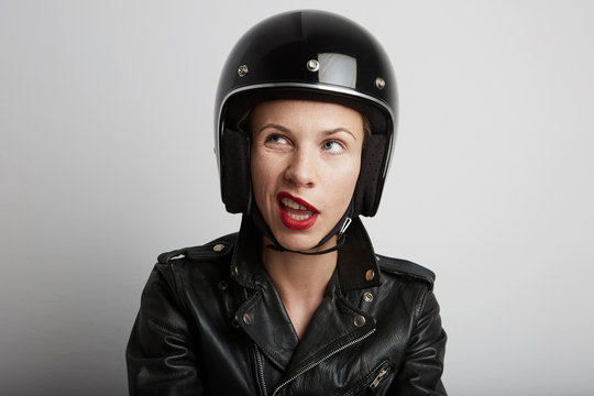 Portrait of biker woman over white background, female with funny face wearing stylish black sportive helmet and leather jacket.