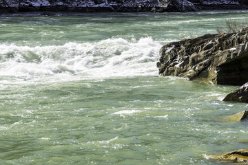 River rapids with white waves flowing, snow and ice on rocky riverbank