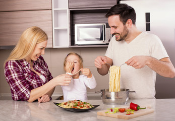 Obraz na płótnie Canvas Young couple with kid having fun in kitchen while preparing spaghetti 