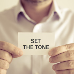 Businessman holding SET THE TONE message card