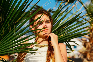 attractive brunette woman in a white dress standing on a background of palm leaf
