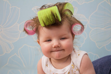 The baby smiles with curlers in her hair.
