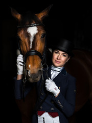 Fototapeta na wymiar Horsewoman in uniform with a brown horse over dark background.