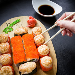Sushi rolls and sauce and woman hand with chopsticks on black background. Traditional Japanese food. Flat lay. Top view.
