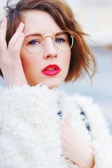 portrait of a young pensive beautiful woman with bright makeup, with glasses and a white sweater outside on a Sunny day