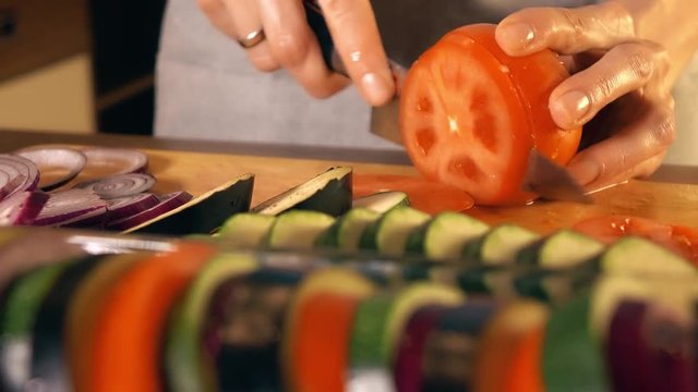 Young woman cutting juicy red tomato. Cooking homemade ratatouille. 4K close-up video
