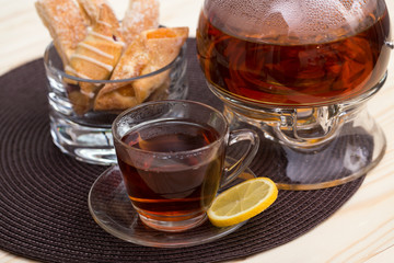 A pot of tea on the heater, and a cup of tea with lemon on a brown cushion table with cakes