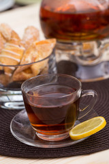 A pot of tea on the heater, and a cup of tea with lemon on a brown cushion table with cakes