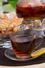 A pot of tea on the heater, and a cup of tea with lemon on a brown cushion table with cakes
