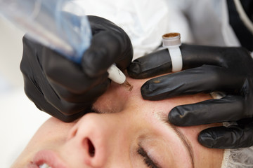 beautiful young lady getting tattoo. professional tattooist making eyebrow make up