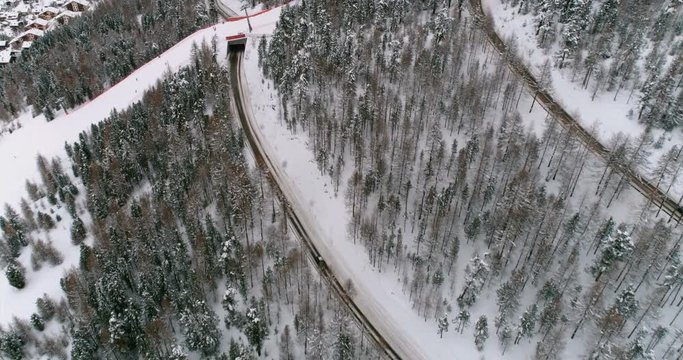 Flying above trees and road with tunnel under ski lift, winter snow season