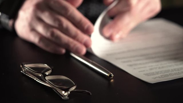 Close up shot of the manager hands, who signed the contract on the conclusion of the agreement between the agencies. Likely a man works hard, so began to see badly and wears glasses. Selective focus.