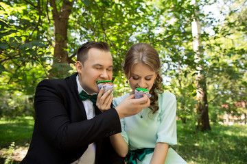 Man and woman eating green cupcakes in park. Green wedding or saint patrick day. Couple in love with sweets