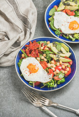 Healthy breakfast with fried egg, chickpea sprouts, seeds, vegetables and greens in bowls over grey background, selective focus. Clean eating, healthy lifestyle, detox, vegetarian food concept