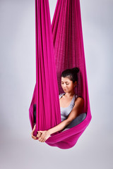 Young woman practices aerial different inversion yoga with a hammock in a white studio. Concept of...