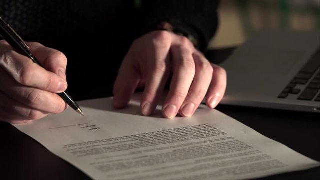 Close up shot of man's hands, who leaves signature on the agreement. Man carefully writes the initials of the client's name in the appropriate column. Signature is fake.