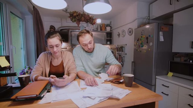 Sad young couple paying the bills. Man and woman sitting in the kitchen and sorting checks and accounts.