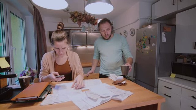 Young couple calculating their domestic budget together in the kitchen, try to safe money, having stresses.