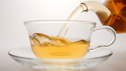 Fresh tea flows in a tea cup from a teapot