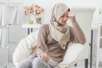 young asian woman hold her head thinking about something while sitting on a couch