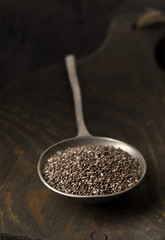 Raw unprocessed black chia seeds in metal spoon on wooden board