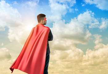 A businessman in superman cape standing turned back on the sky background