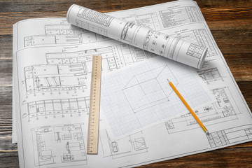 A set of open and rolled up blueprints on wooden table background with a pencil and a ruler lying beside.