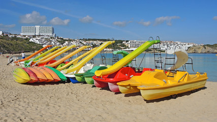 Group of colorful pedal boats with and without slide on the beach of Arenal d'en Castell, Menorca Island, Spain.