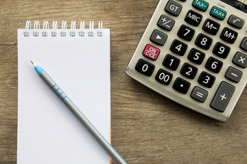 Top view of note book with pen and calculator on wooden table background