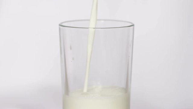 Milk pouring into a glass on white background, slow motion.