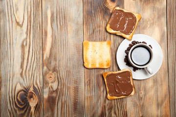 cup with coffee, toast and chocolate on wooden table