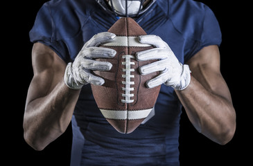 Close up view of an American Football player holding a football. Selective focus on the laces of the football and the wide receiver gloves. Shot on a black background