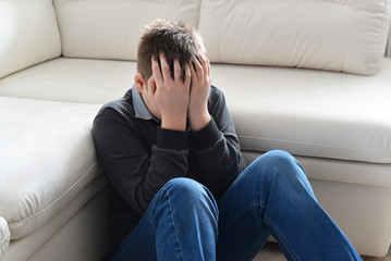 Upset teenager 13 years, he sits near sofa covering her face with her hands