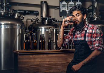 Indian male manufacturer tasting craft beer in the microbrewery.