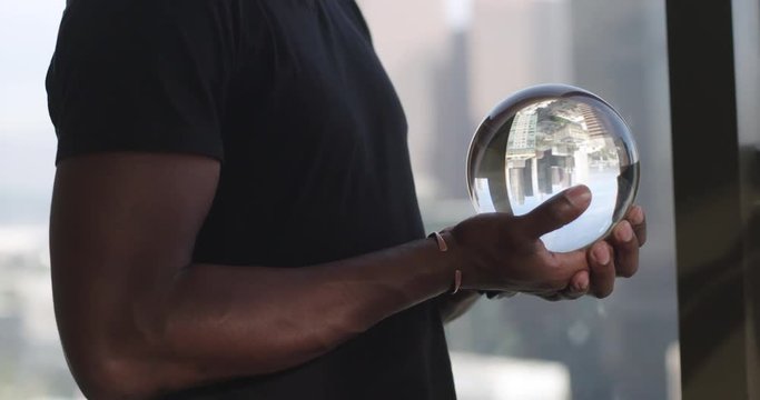 African American man's hands holding a crystal ball in front of Downtown Los Angeles skyline.  Big close up, recorded hand-held in real time.