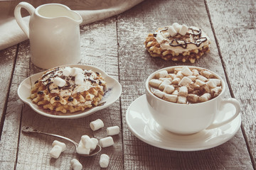 White cup of coffee with milk, marshmallow and homemade waffle with whipped cream with decor on top. Tasty breakfast. Vintage toned.