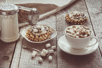 White cup of coffee with milk, marshmallow and homemade waffle with whipped cream with decor on top. Tasty breakfast. Vintage toned.