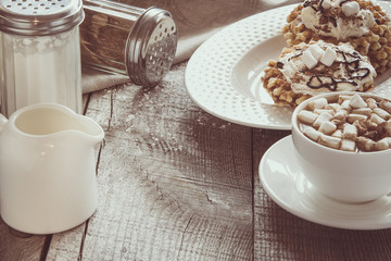 White cup of coffee with milk, marshmallow and homemade waffle with whipped cream with decor on top. Tasty breakfast. Vintage toned.