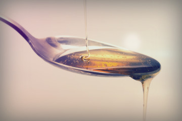 Honey pouring from spoon against a light background