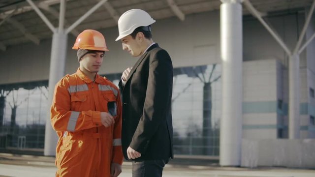 Man in a suit giving to the construction worker in uniform an envelope with money bribe. Happy worker hiding money. Corruption deal. Slowmotion