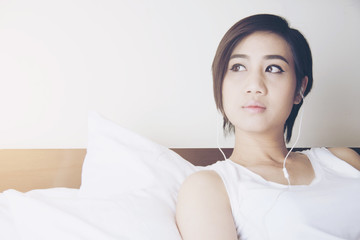 Beautiful Asian women wear white shirt and listen music on the bed.