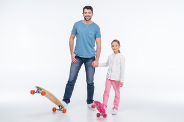 smiling father and daughter standing with skateboards on white