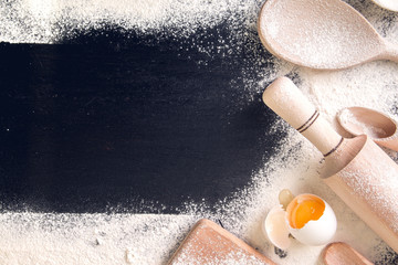 Copy space around utensils, flour and egg on black background. Top view. Frame. Ingredients and tools for baking.