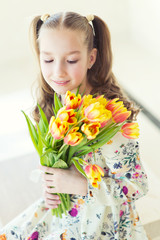 Beautiful toddler girl sitting in the room with fresh tulips, smiling with happy face, waiting for spring and Easter holidays