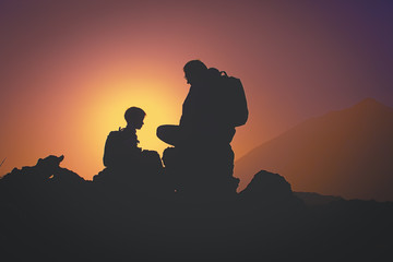Silhouettes of father and son travel in sunset mountains
