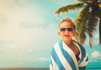 happy little boy wrapped in towel at beach