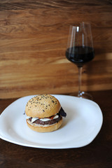Burger and a glass of red wine on a wooden background. Free space for design